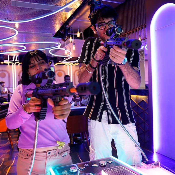 Two young adults play a laser tag game in a dimly lit, neon-lit arcade.