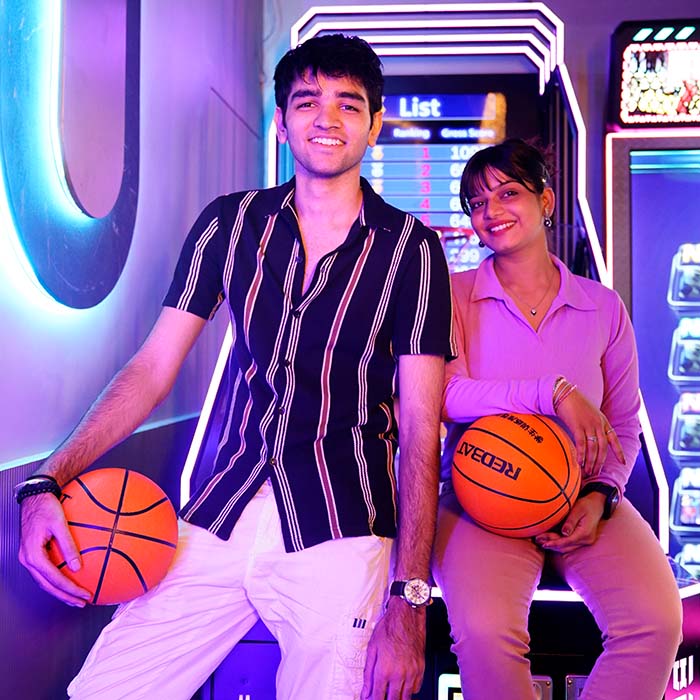 A young couple poses with basketballs in an arcade.