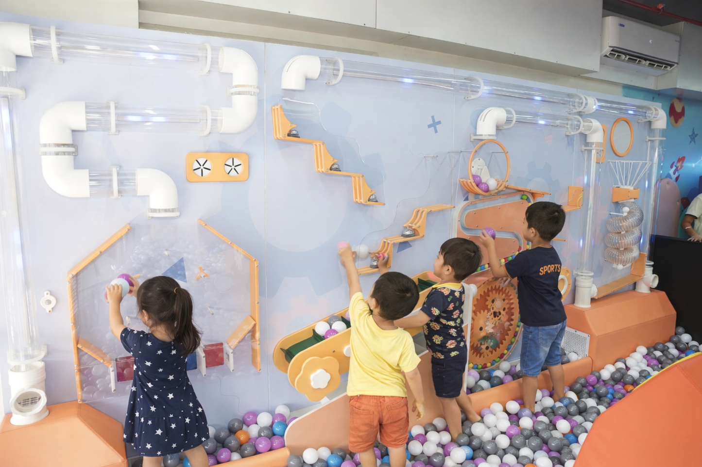 Children play with balls and tubes in a colorful indoor playground.