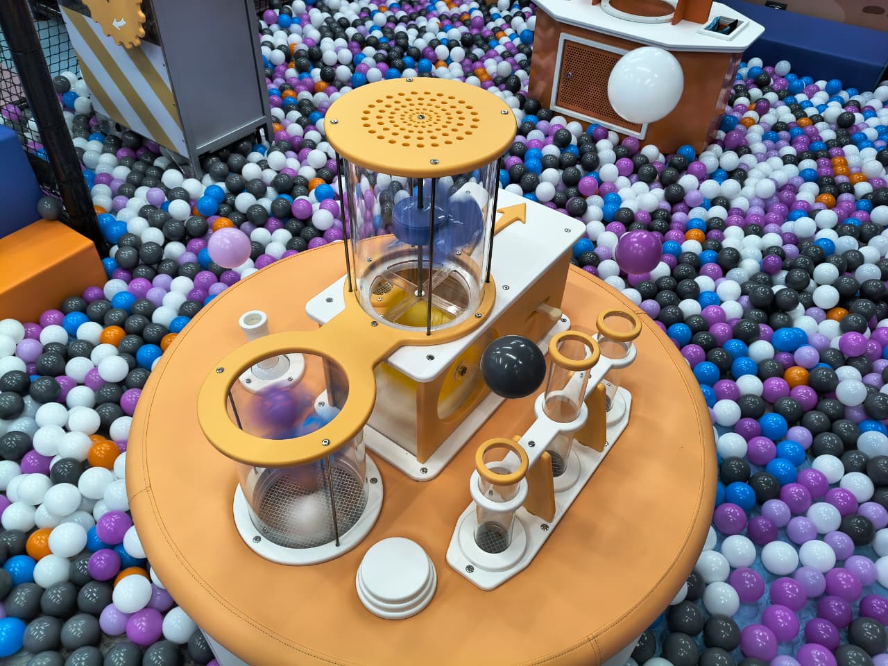 Children play in a ball pit with a colorful science-themed interactive toy.
