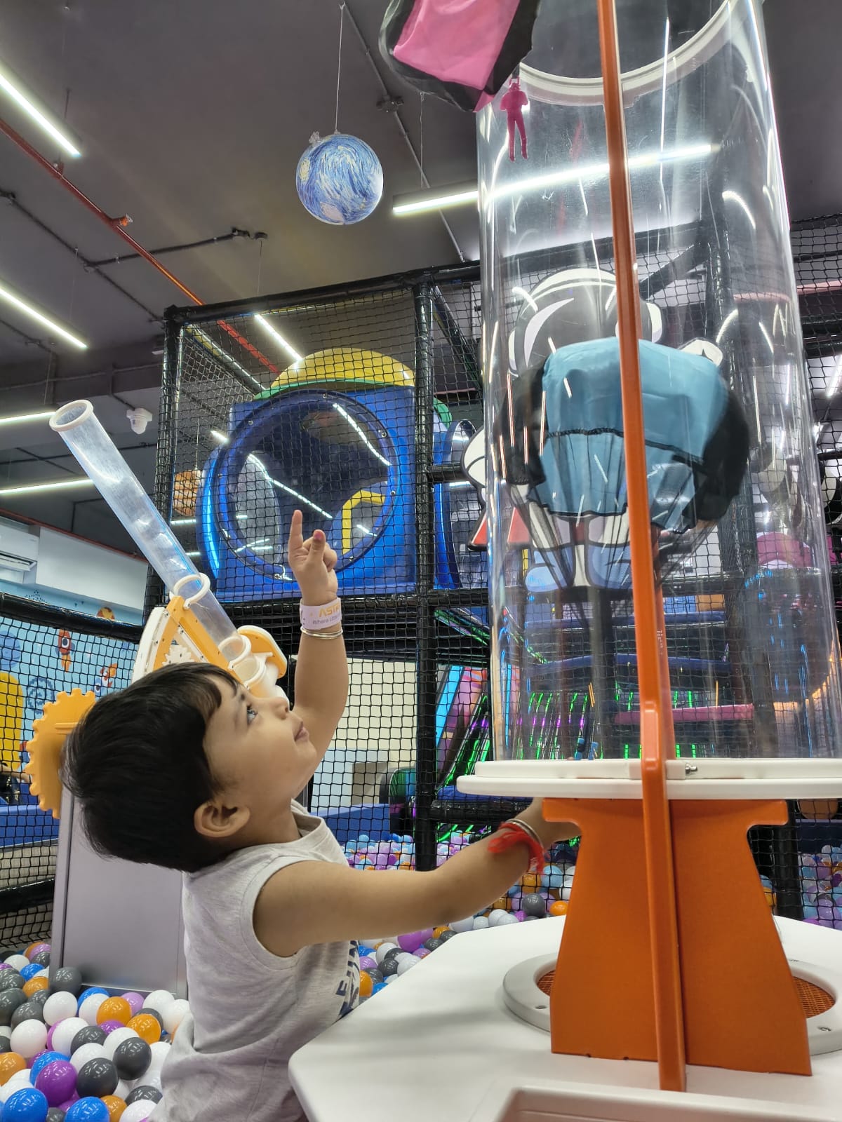 A young child points up at a globe hanging in a colorful indoor playground.
