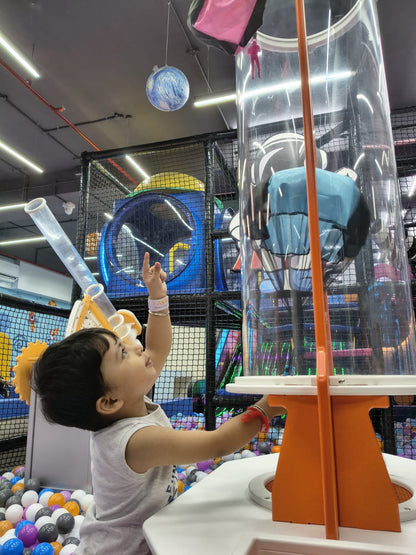 A young child points up at a globe hanging in a colorful indoor playground.