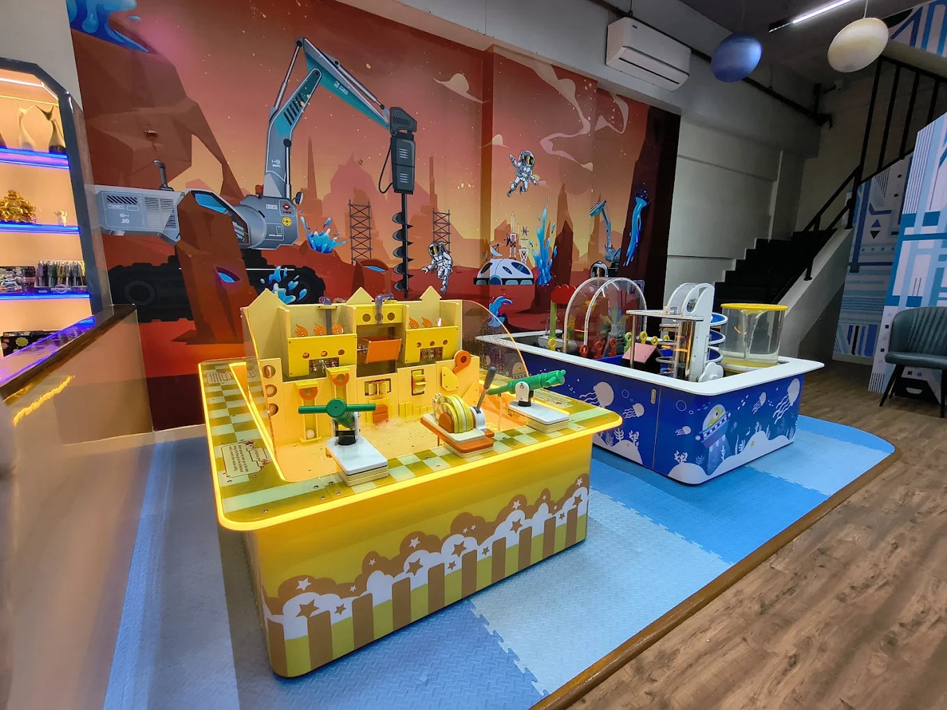 Children's interactive play area with a space-themed mural and water play tables.