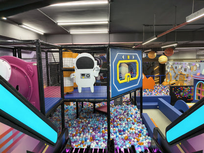 An indoor playground with a ball pit, slides, and space-themed decorations. Children can be seen playing in the ball pit.