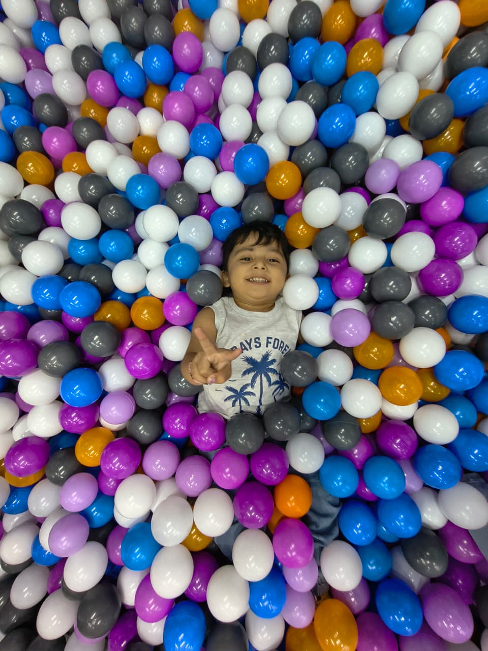 A young child smiles while lying in a ball pit filled with colorful balls.