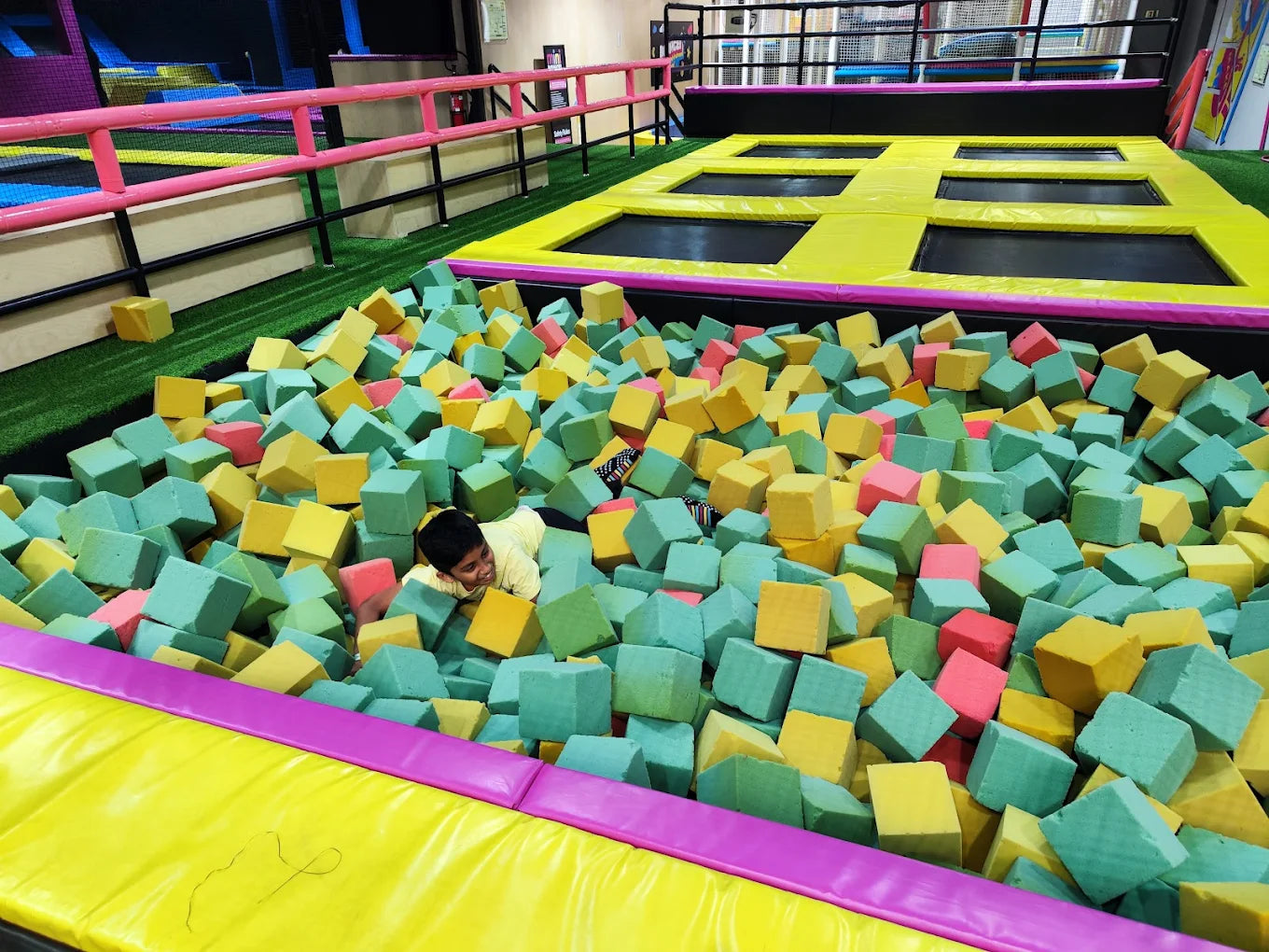 A young boy smiles while playing in a foam pit filled with colorful cubes at a trampoline park.