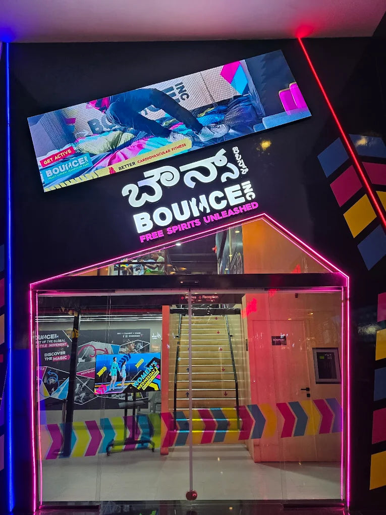 A brightly lit indoor trampoline park entrance with a large "BOUNCE!" sign and a staircase.