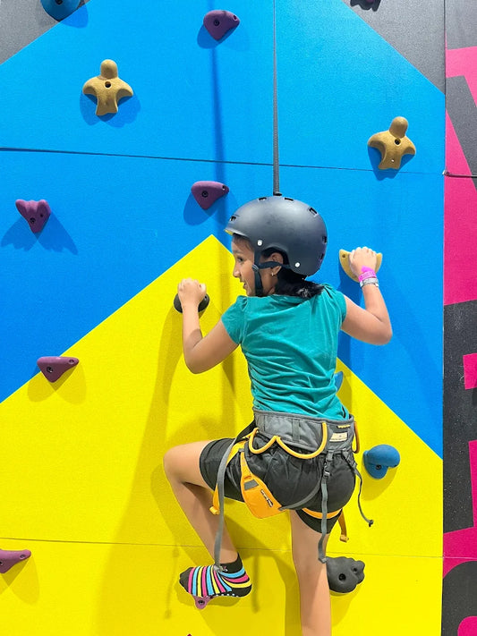 A young child in a helmet climbs a colorful indoor rock wall.