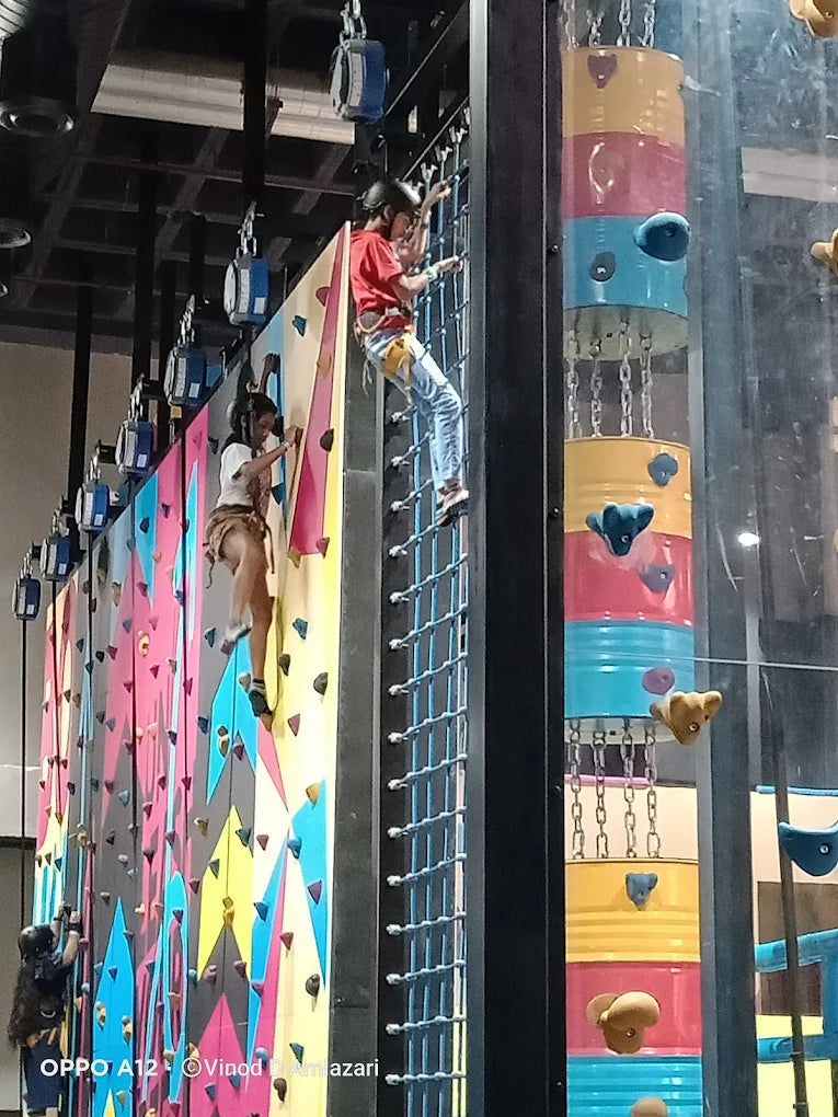 Two children climb a colorful indoor rock-climbing wall.