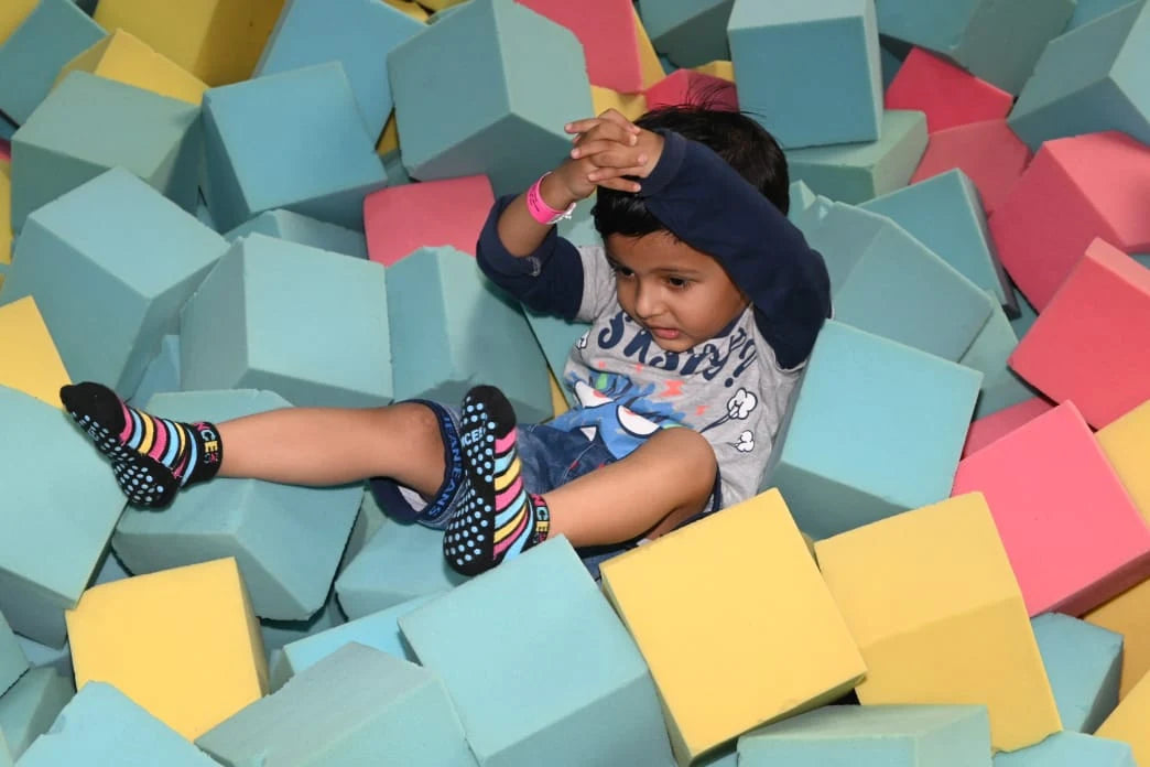 A young child sits in a ball pit filled with colorful foam cubes.
