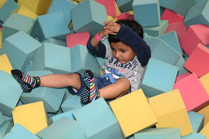 A young child sits in a ball pit filled with colorful foam cubes.