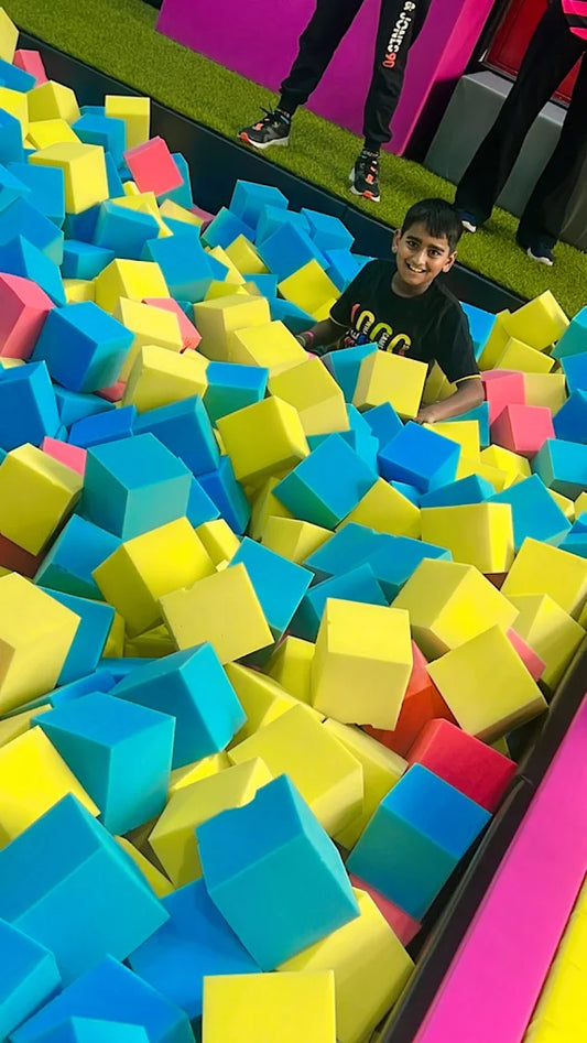A young boy smiles while playing in a foam pit filled with colorful cubes.