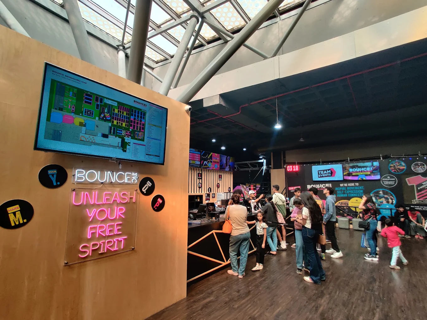 People gather at the entrance of an indoor trampoline park, with a map displayed on a screen and neon signs.