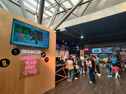 People gather at the entrance of an indoor trampoline park, with a map displayed on a screen and neon signs.
