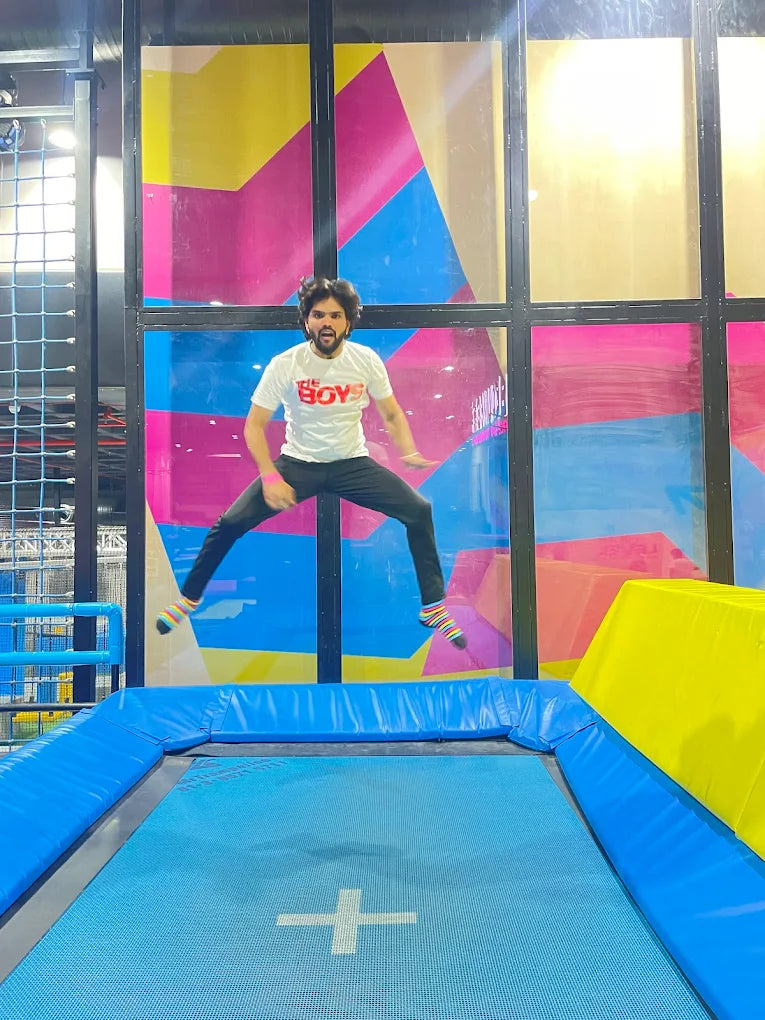 A young man jumps on a trampoline in a colorful indoor play area.