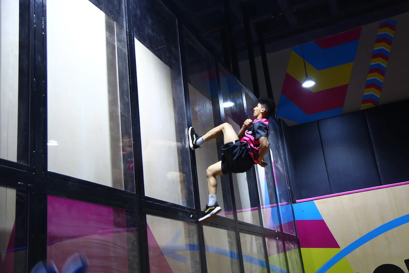 A young person performs a flip on a trampoline wall in a colorful indoor park.