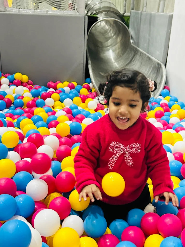 A young child plays in a ball pit with a slide in the background.