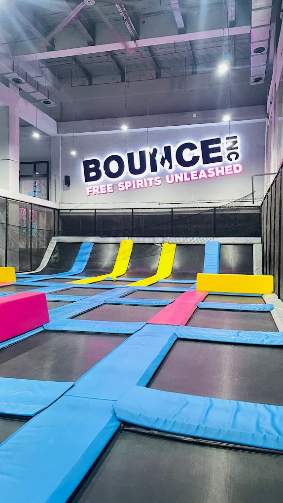 An indoor trampoline park with colorful padded areas and a "Bounce Inc." sign.