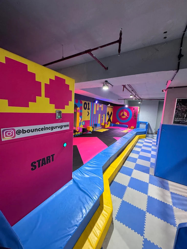 An indoor trampoline park with colorful padded walls and a checkered floor.