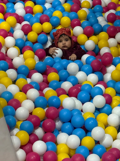 A baby wearing a red hat sits in a ball pit filled with colorful balls.