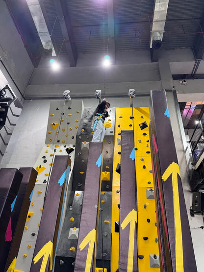 A child climbs a colorful indoor rock wall, secured by a harness and rope.
