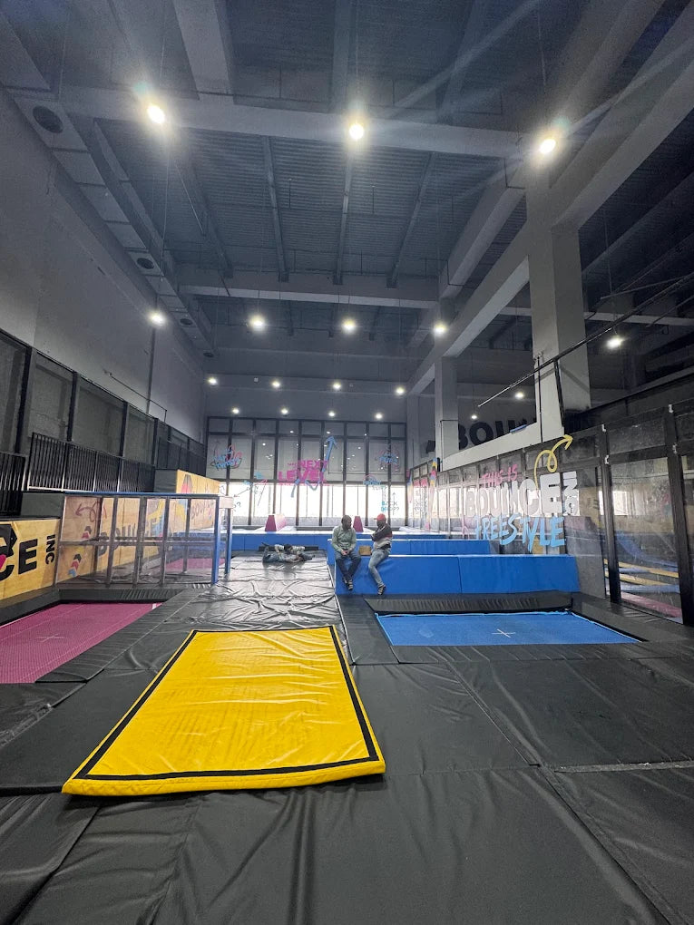 An indoor trampoline park with several trampolines and two young adults sitting on the edge.