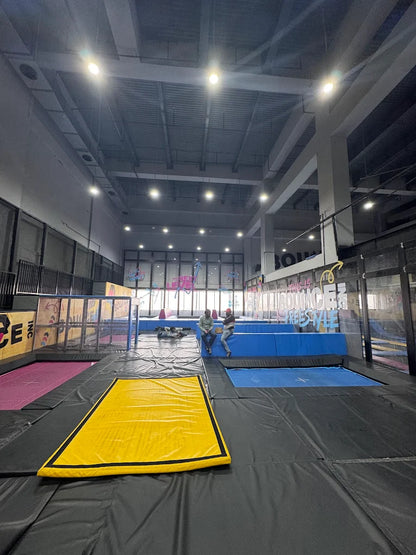 An indoor trampoline park with several trampolines and two young adults sitting on the edge.
