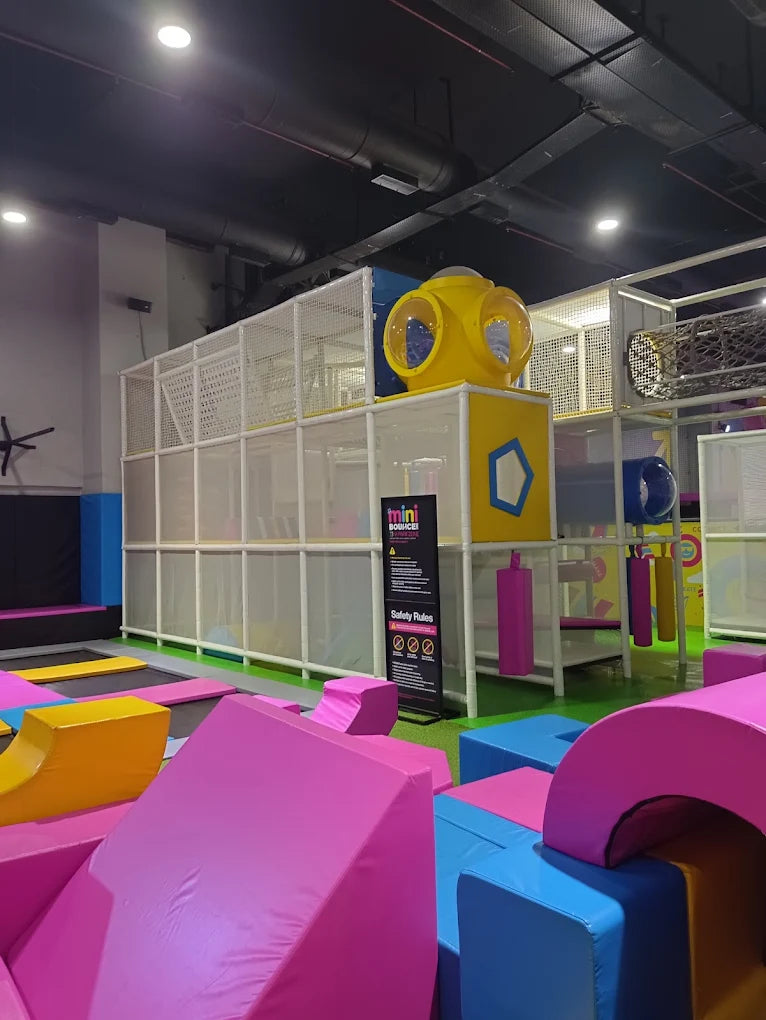 A colorful indoor playground with trampolines and soft play structures for children.