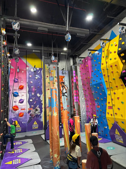 Young people climb colorful indoor rock walls with safety harnesses.