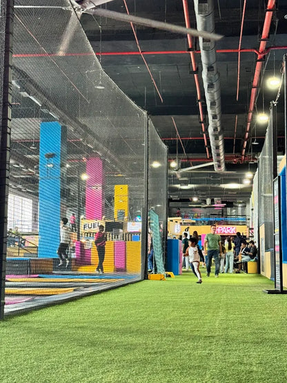 People enjoy a trampoline park with colorful walls and a green turf floor.