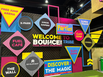 A colorful wall at a trampoline park with signs for various activities like "Free Jump Arena" and "Slam Dunk."