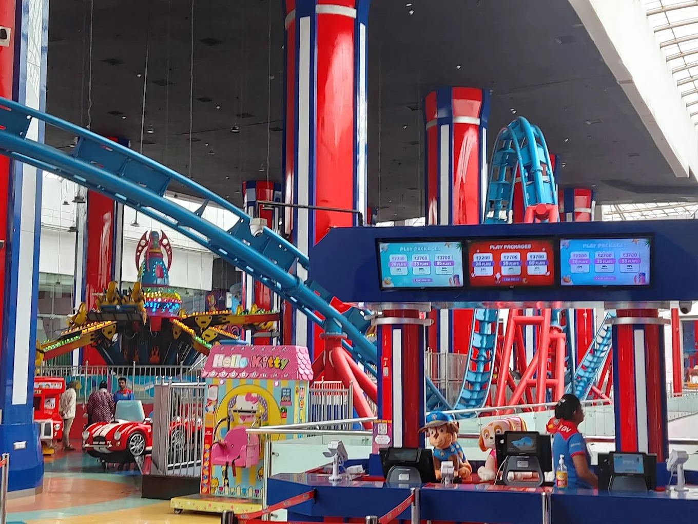 An indoor amusement park with a roller coaster, rides, and ticket booths staffed by young adults.