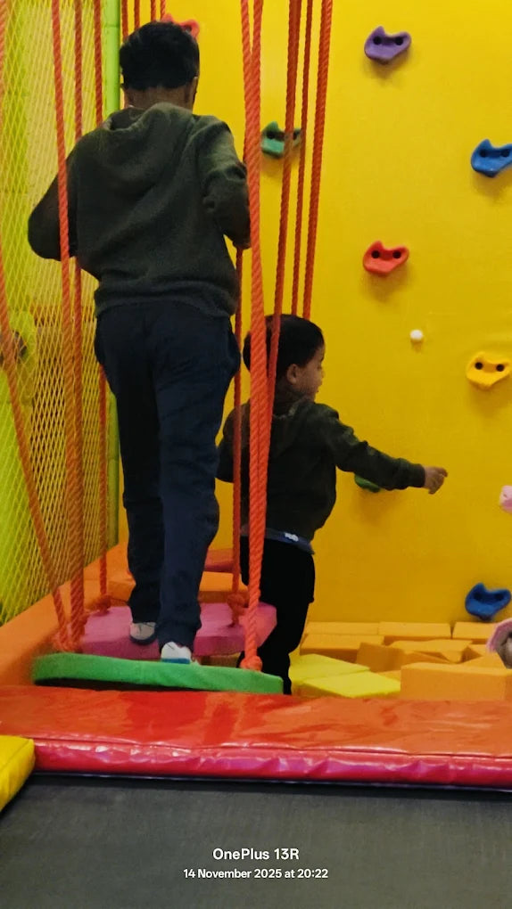 A man and a child climb on a colorful indoor obstacle course with a yellow climbing wall.