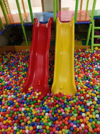 Two colorful slides descend into a ball pit filled with children's toys.