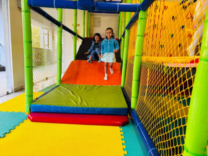 Two young girls slide down a colorful indoor playground slide.