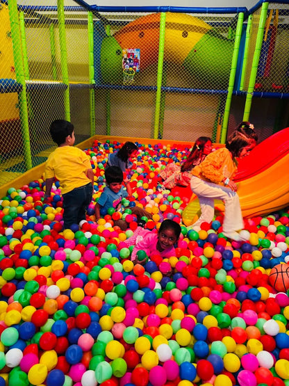 Children play in a colorful ball pit at an indoor playground.