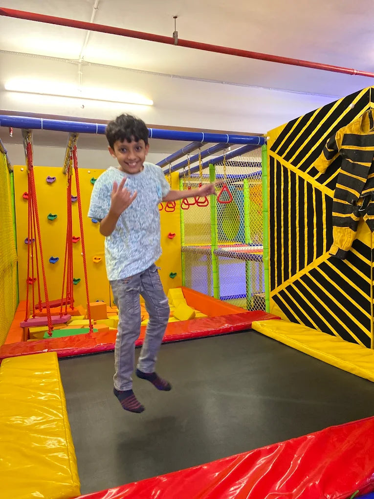 A young boy jumps on a trampoline in an indoor play area.