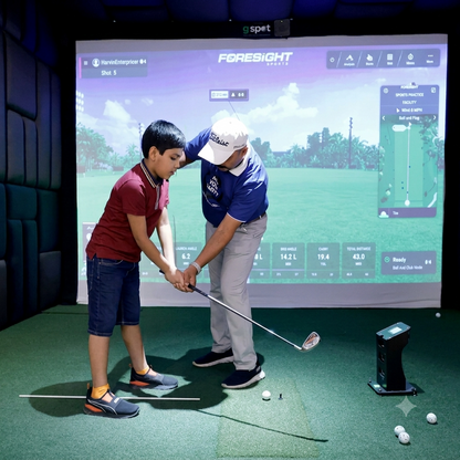 A young boy and an adult man practice golf indoors on a simulator.