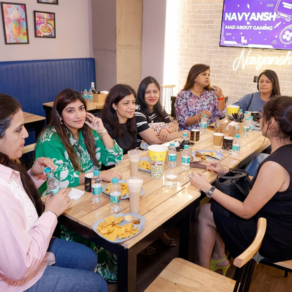 A group of young women sit at a table in a cafe, enjoying drinks and snacks.