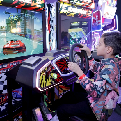 A young boy plays a racing arcade game, gripping the steering wheel as a virtual car speeds across the screen.