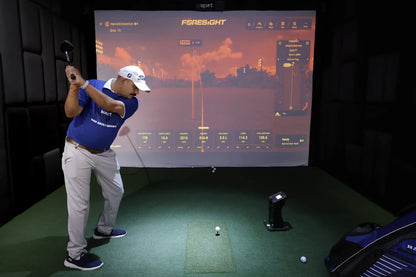 A man plays golf indoors on a simulator, with a screen displaying his shot data.