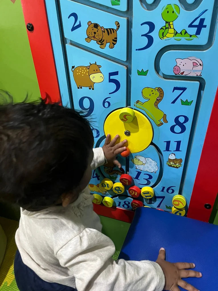 A baby plays with a colorful wooden activity board featuring numbers and animals.