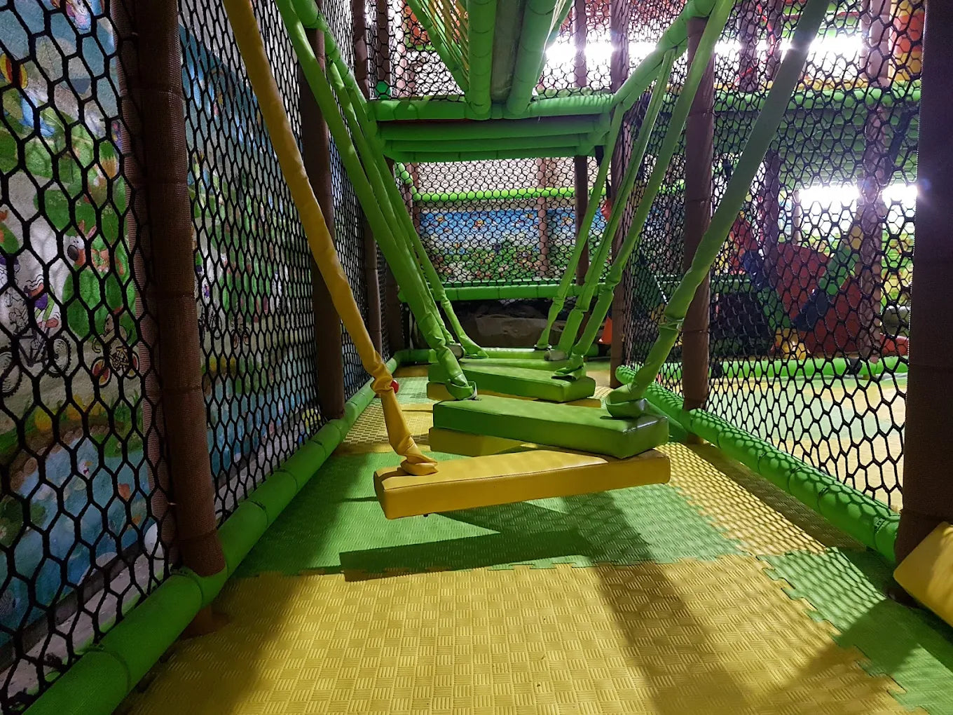 A colorful indoor playground with rope bridges and soft flooring.