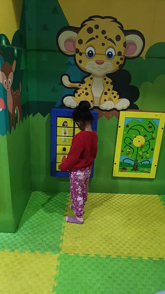 A young child plays with interactive wall panels in a colorful, jungle-themed play area.