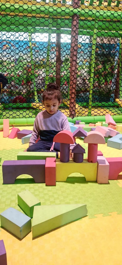 A young child plays with colorful foam blocks in a soft play area.