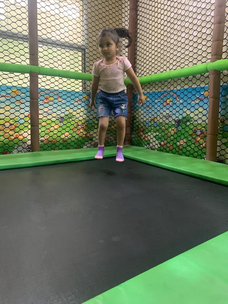 A young girl jumps on a trampoline in an indoor play area.