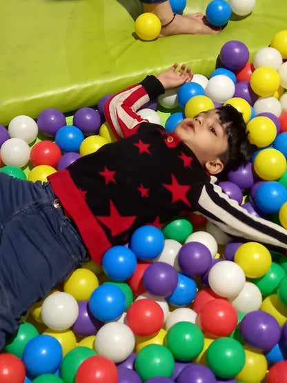 A young child lies in a ball pit, surrounded by colorful balls.