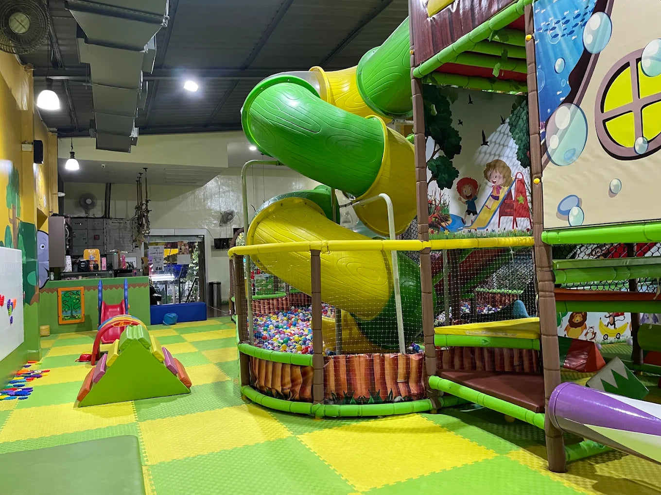 A colorful indoor playground with slides, a ball pit, and soft play structures for young children.