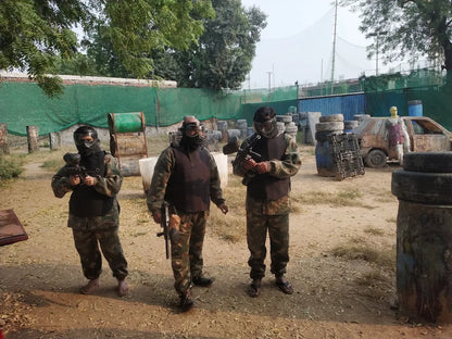 Three young adults in camouflage gear and masks stand ready for a paintball game in an outdoor arena.