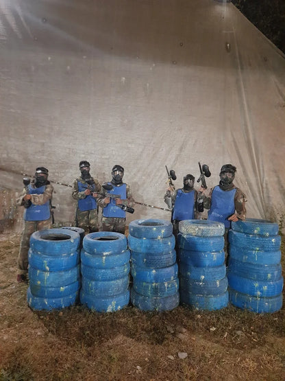 Paintball players in protective gear stand behind stacks of blue tires.